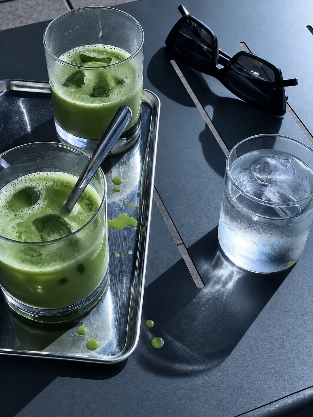 暗いテーブルの上のアイス抹茶二杯、サングラスと水のグラス